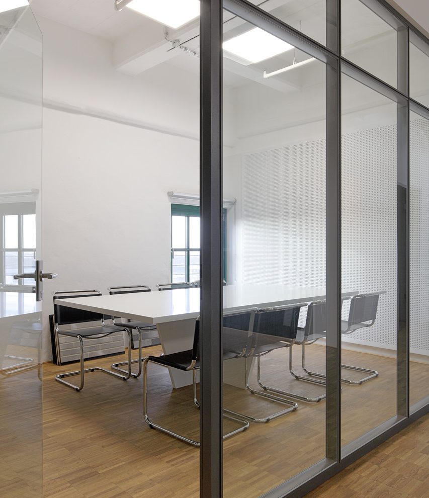 Moderner Besprechungsraum mit Glastrennwand und acht Stühlen.