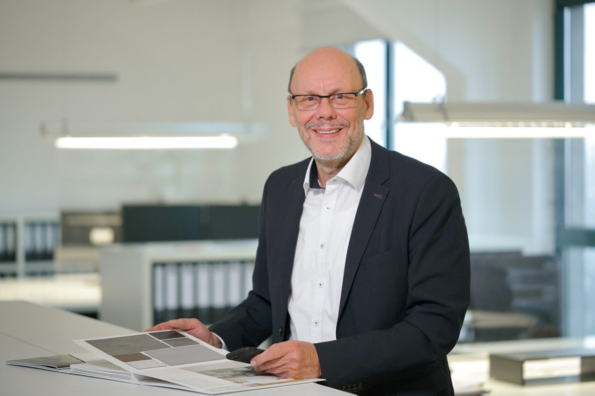 Mann im Anzug lächelt und blättert in Materialmustern im Büro