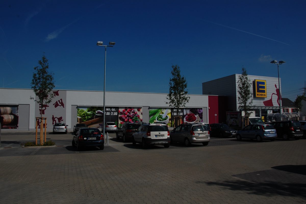 Flacher Supermarktbau mit großformatigen Werbegrafiken und Parkplatz.