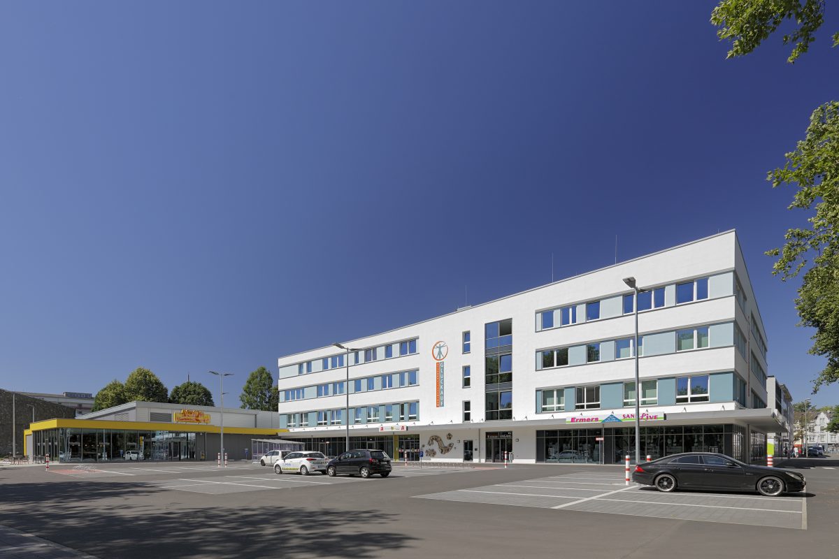 Modernes Ärztehaus mit Apotheke und großem Parkplatz davor.