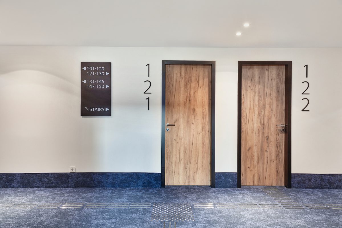 Hotelflur mit Teppichboden, Holztüren und klarer Zimmerbeschilderung.