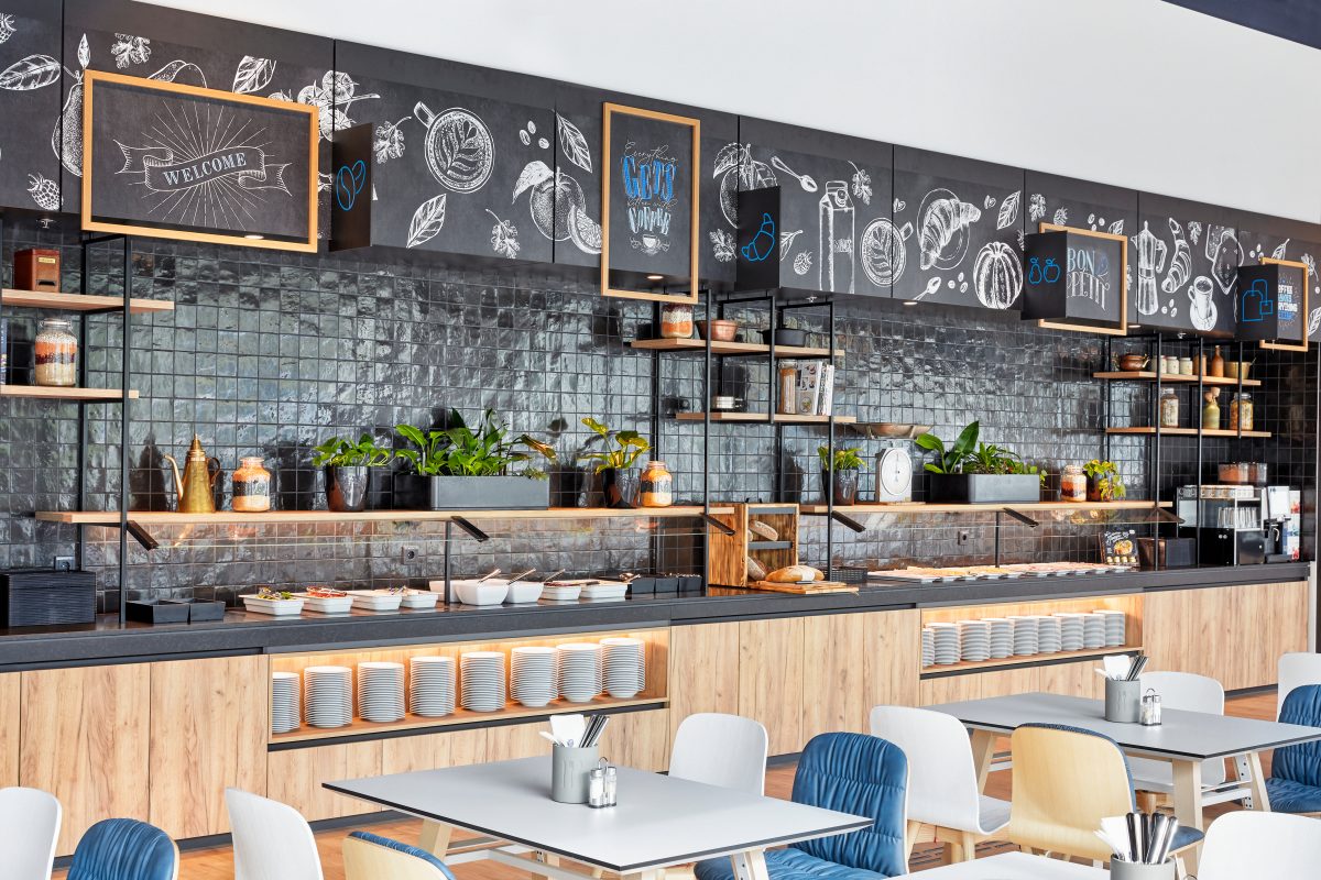 Frühstücksbuffet in modernem Hotel mit Pflanzen, Tafeldekor und offener Küche.