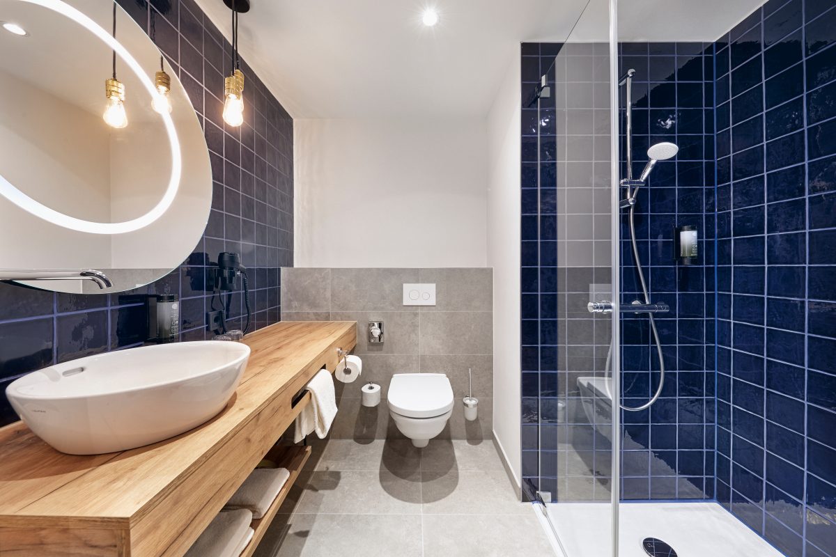 Modernes Hotelbad mit Hänge-WC, Glasdusche und Waschtisch aus Holz.