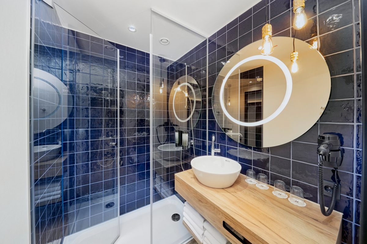 Modernes Hotelbad mit runder Spiegelbeleuchtung, Waschtisch und Glasdusche