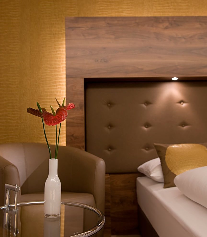 Modernes Hotelzimmer mit gepolstertem Betthaupt, Ledersessel und stilvoller Vase.