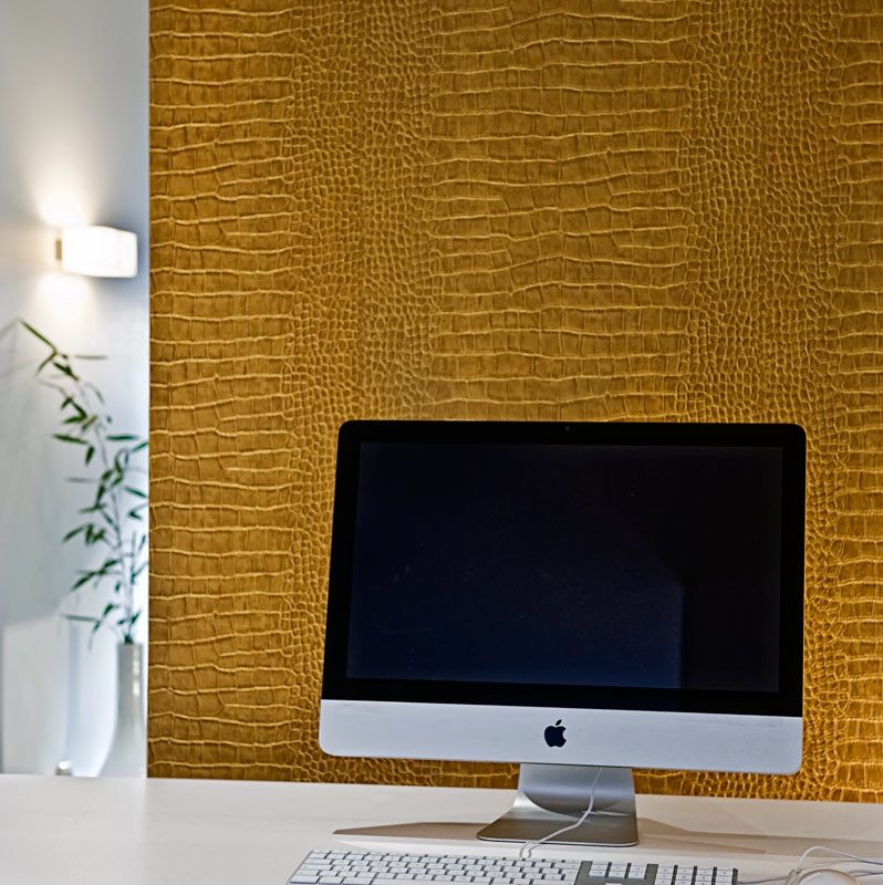 Moderner Arbeitsplatz mit iMac vor strukturierter goldbrauner Krokodiloptik-Wand.
