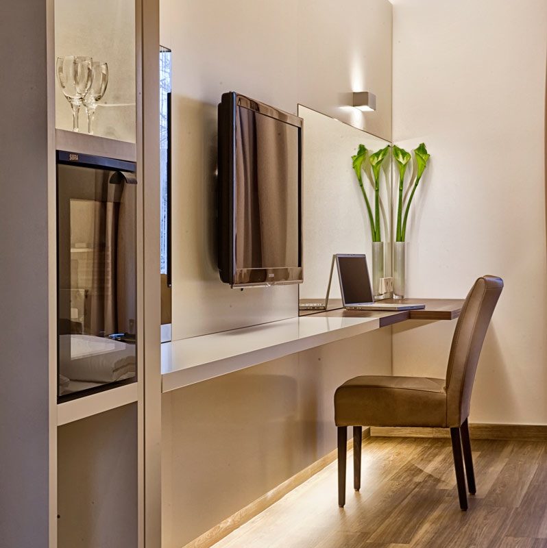 Eleganter Arbeitsbereich mit Wand-TV, Laptop, Stuhl und Vase mit Callas.