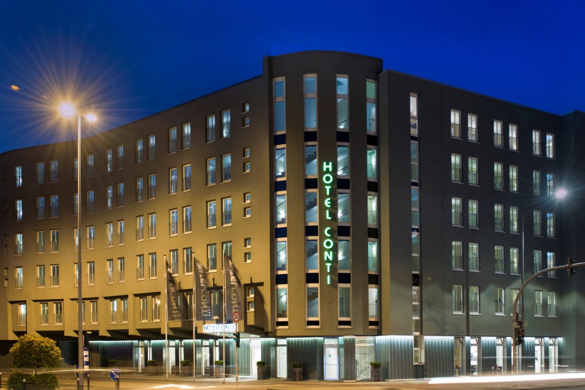 Hotel Conti bei Nacht mit beleuchteter Fassade und grünem Schriftzug.