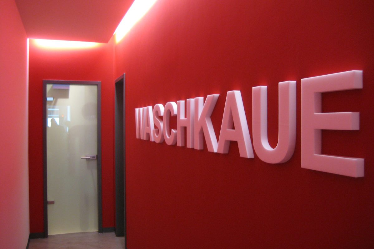 Roter Flur mit beleuchtetem Schriftzug „WASCHKAUE“ an der Wand.