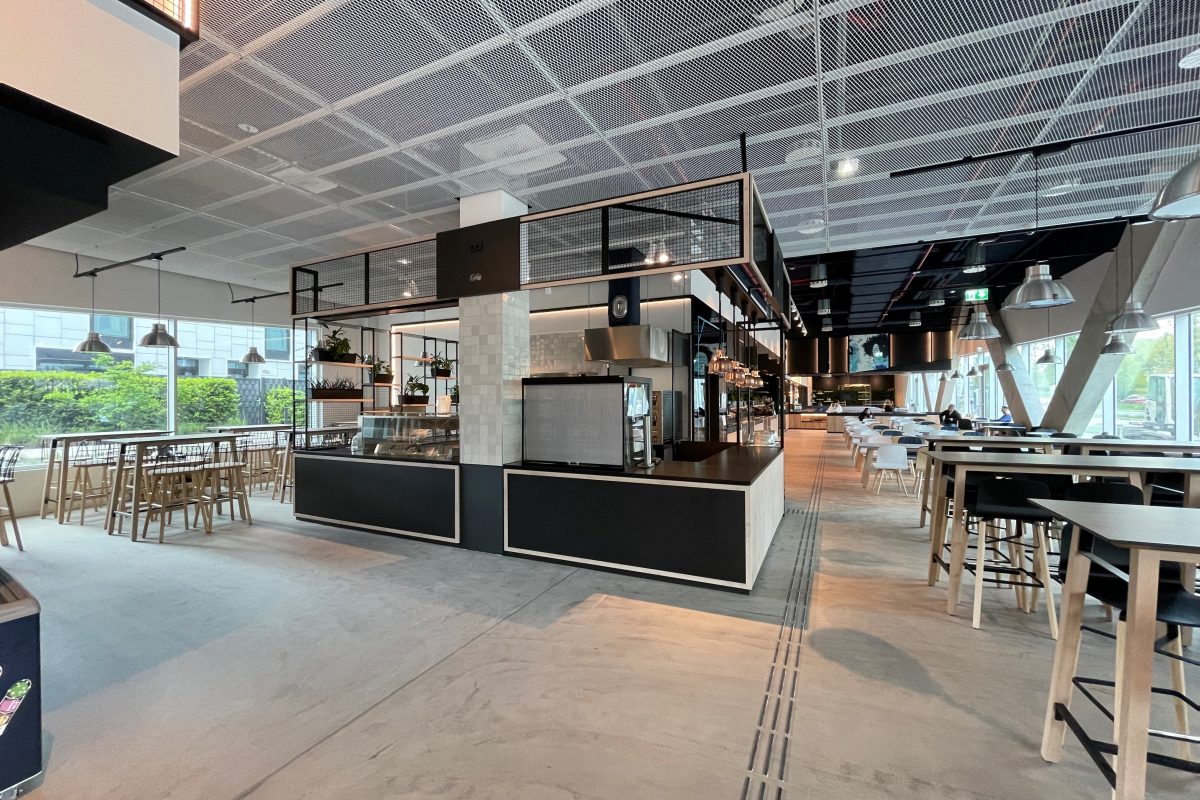 Modernes Hotelrestaurant mit Buffetinsel, großen Fenstern und Holzstühlen.