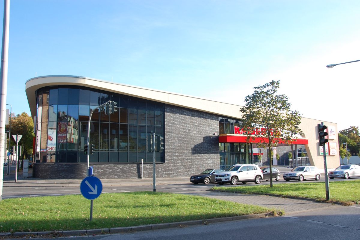 Modernes Supermarktgebäude mit Glasfassade, Klinkeroptik und Parkplatz.