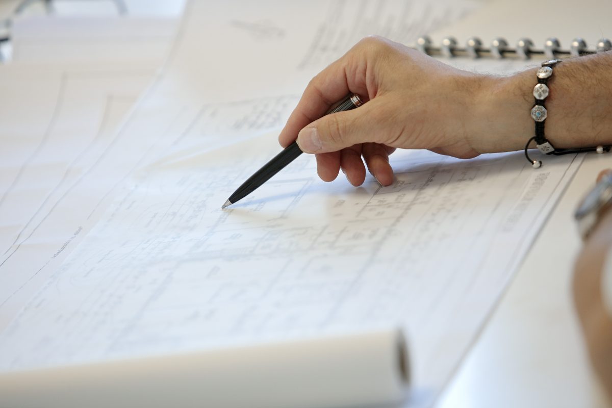 Hand zeigt mit Stift auf technische Zeichnung oder Bauplan.