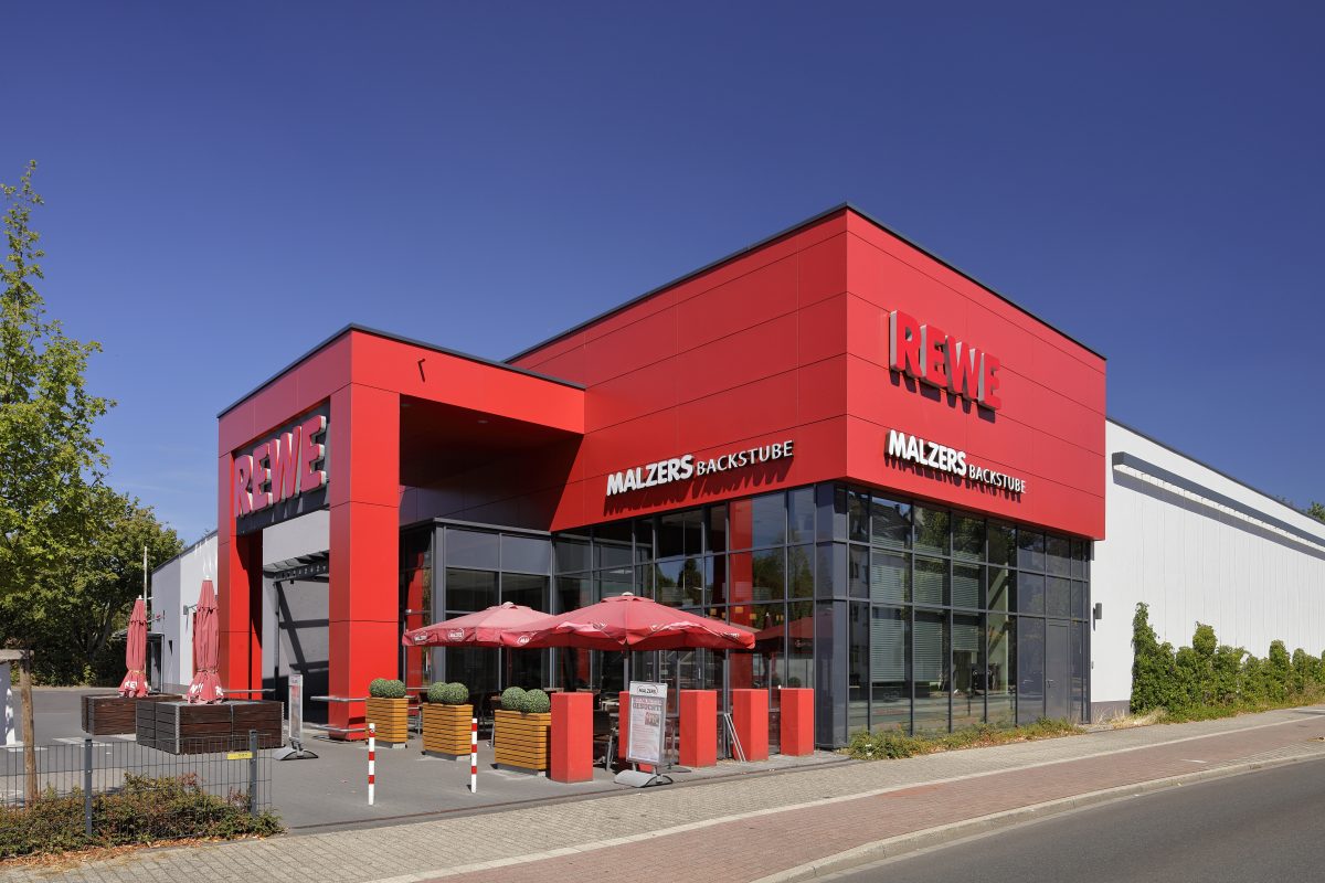 Modernes REWE-Supermarktgebäude mit Bäckerei und Außensitzbereich.