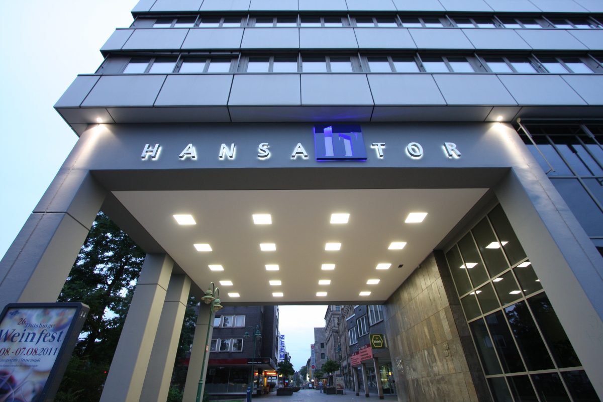 Breiter, beleuchteter Torbogen mit Schriftzug „HANSATOR“ bei Abendlicht.