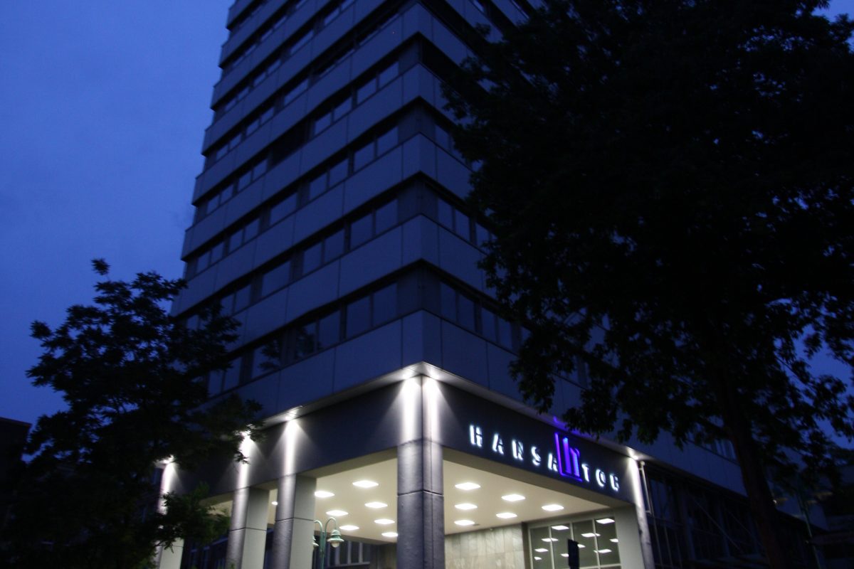 Aufgehende Fassade über Torpassage mit beleuchtetem Schriftzug „HANSATOR“ in der Abenddämmerung.