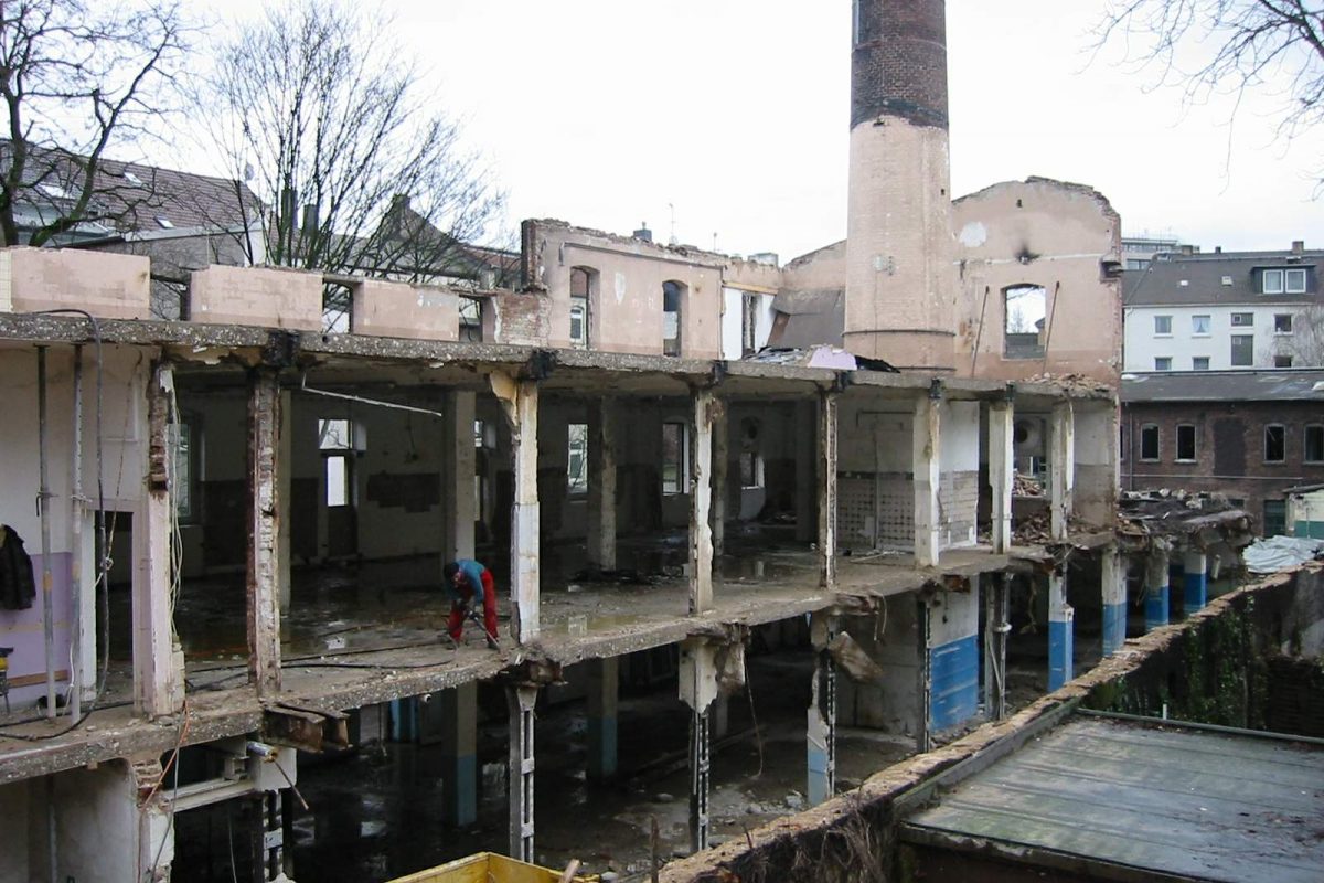 Teilabgerissenes Fabrikgebäude mit Schornstein, freigelegten Etagen und Bauarbeiter.