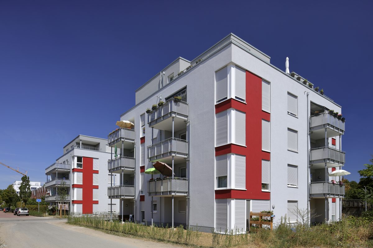 Mehrgeschossiger Neubau mit Balkonen und rot-weißer Fassade.