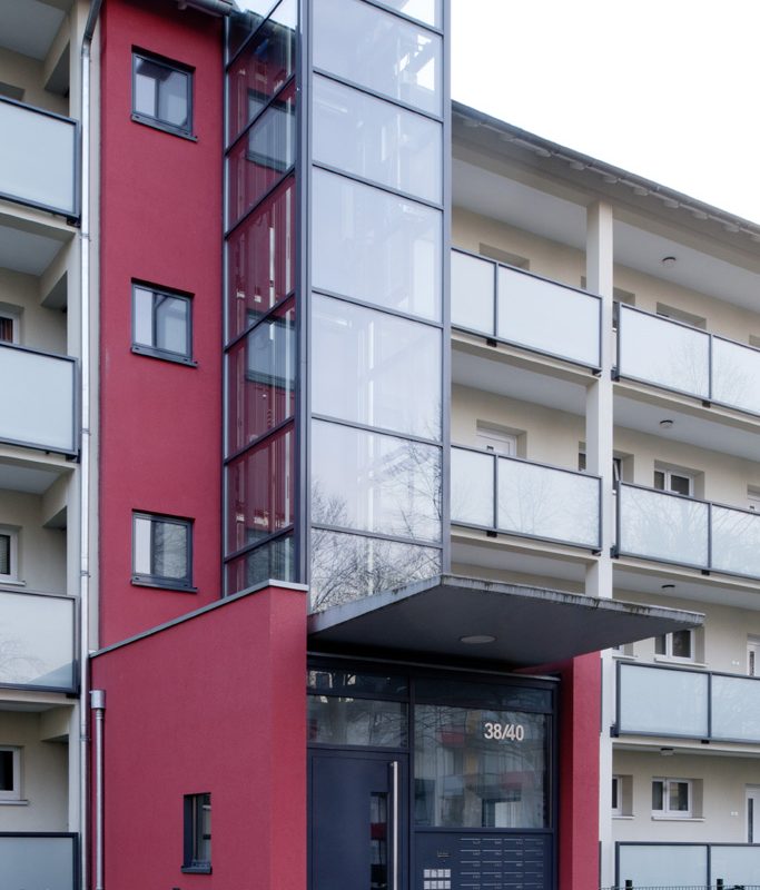 Neuer Glasaufzug vor Bestandstreppenhaus.