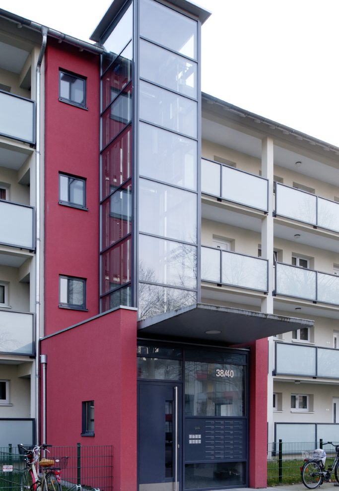 Neuer Glasaufzug vor Bestandstreppenhaus.