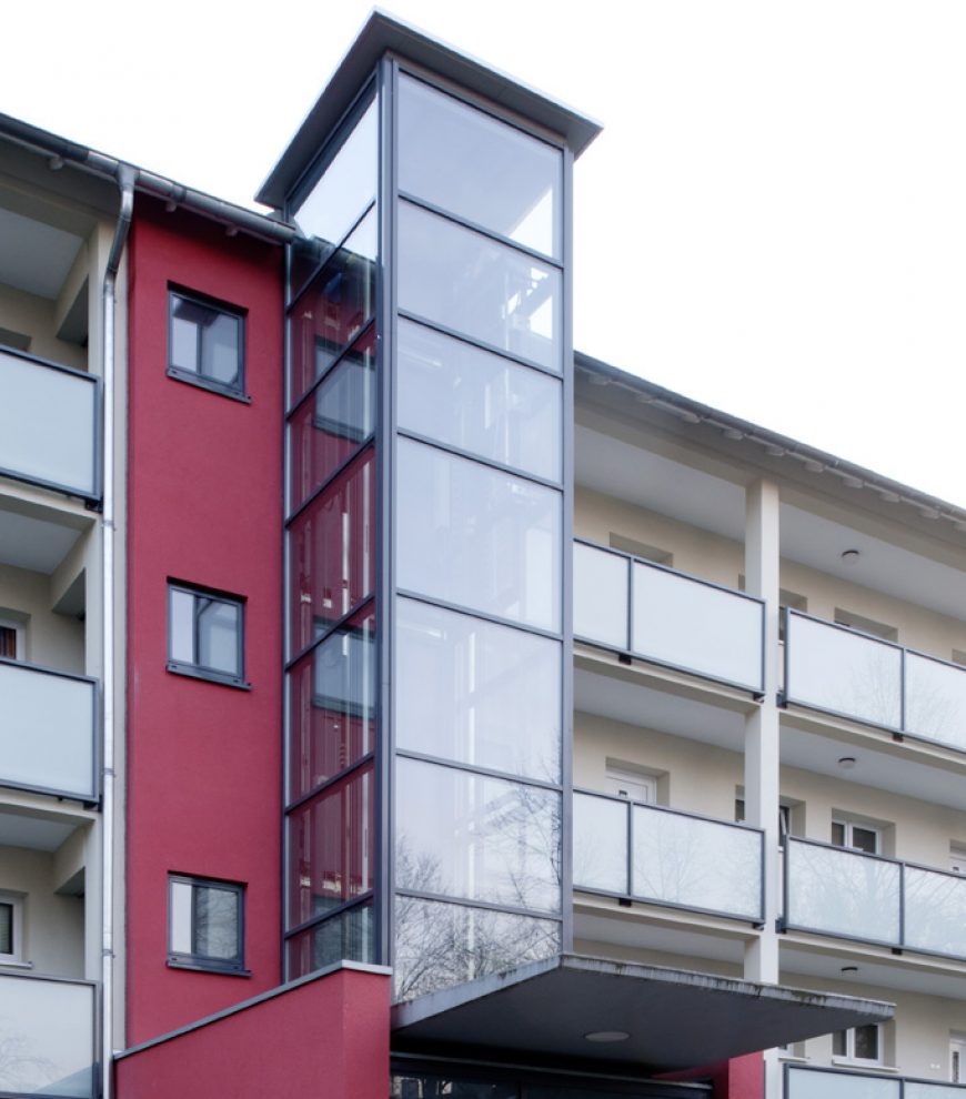 Neuer Glasaufzug vor Bestandstreppenhaus.