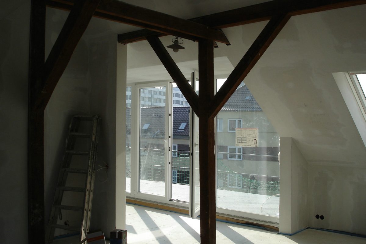 Dachgeschoss im Ausbau mit Balken, großer Fensterfront und Dachterrasse.