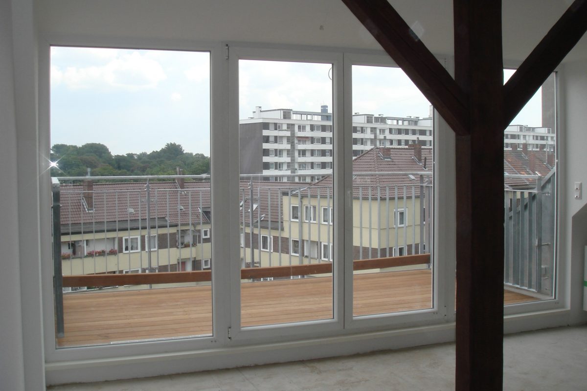 Blick durch große Fenster auf Dachterrasse und Wohnhäuser gegenüber.