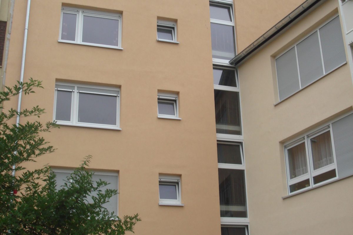 Mehrfamilienhaus mit hellorangefarbener Fassade und weißen Fenstern.