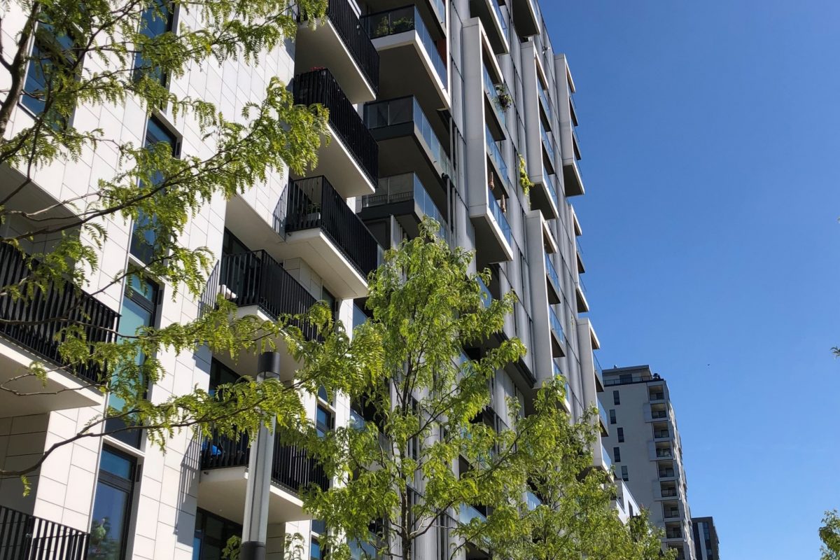 Modernes Wohnhaus mit Balkonen und Bäumen bei blauem Himmel.