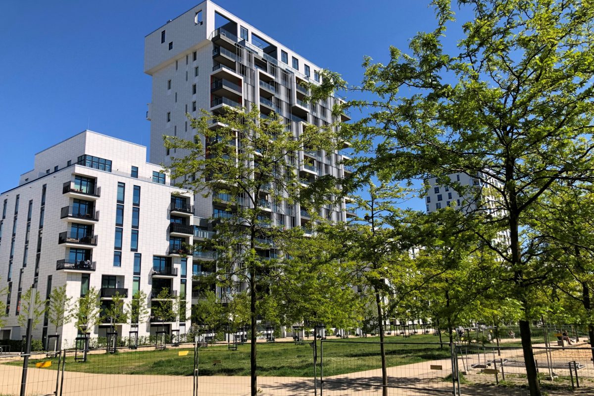 Moderne Wohnhochhäuser mit vorgelagertem Park und jungen Bäumen.