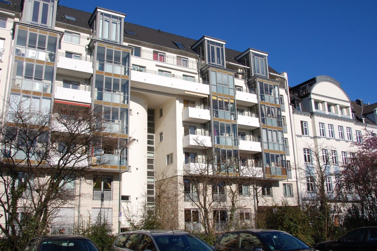 Mehrfamilienhaus mit verglasten Erkern, Balkonen und heller Fassade.