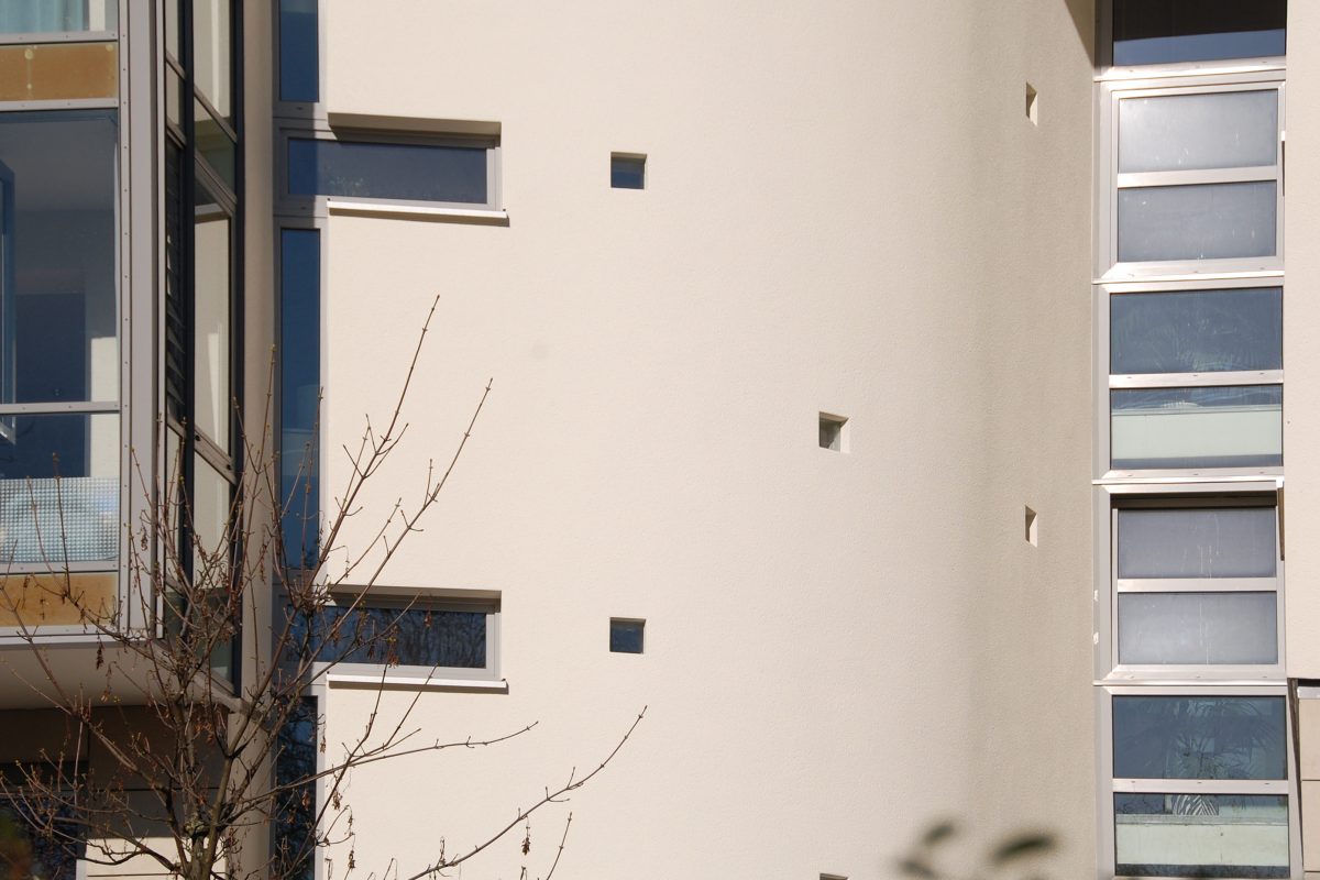 Fassadendetail mit kleinen quadratischen Fenstern und glattem Putz.