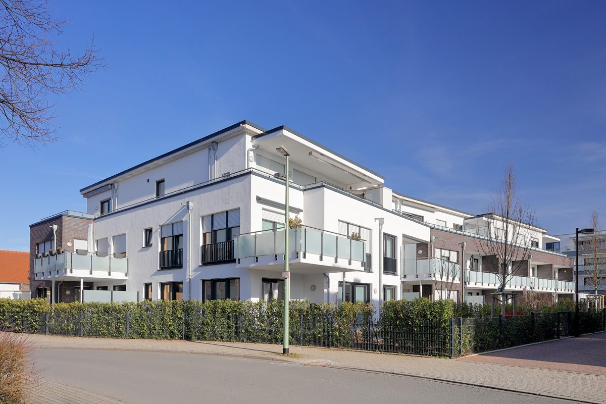 Modernes Eckwohnhaus mit Glasbalkonen und weißer Fassade.