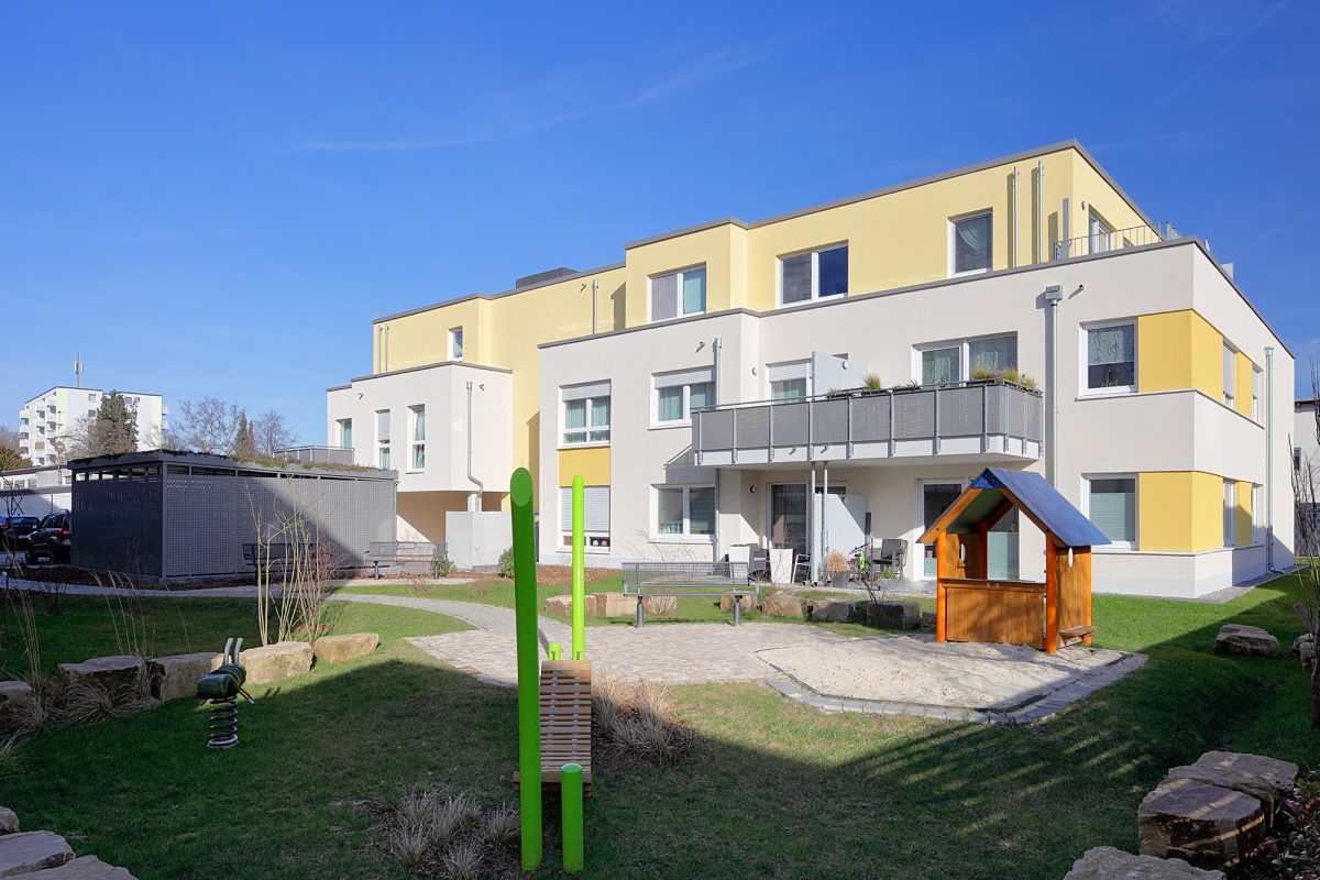 Heller Neubau mit Balkonen und kleinem Spielplatz im Garten.
