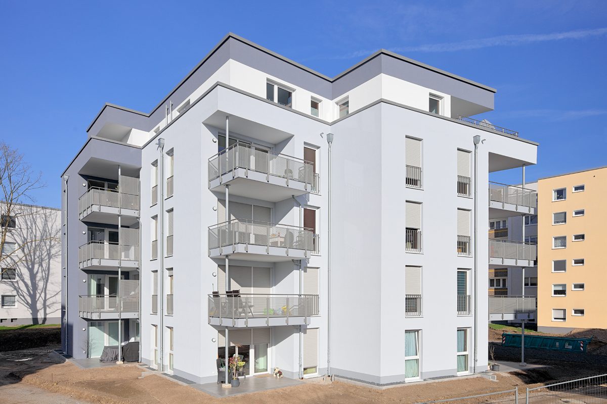 Weißer Neubau mit Balkonen und bodentiefen Fenstern.