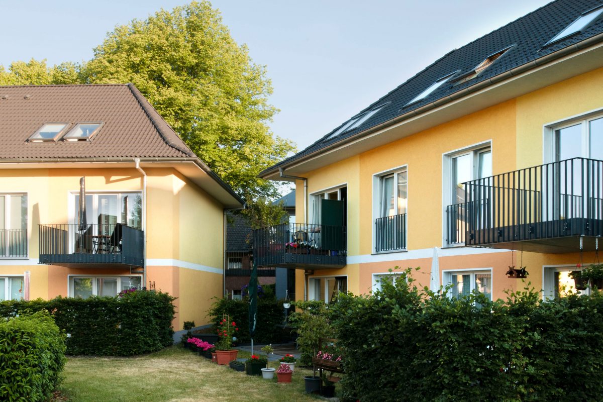 Zwei gelbe Wohnhäuser mit Balkonen und Hecken als Sichtschutz.