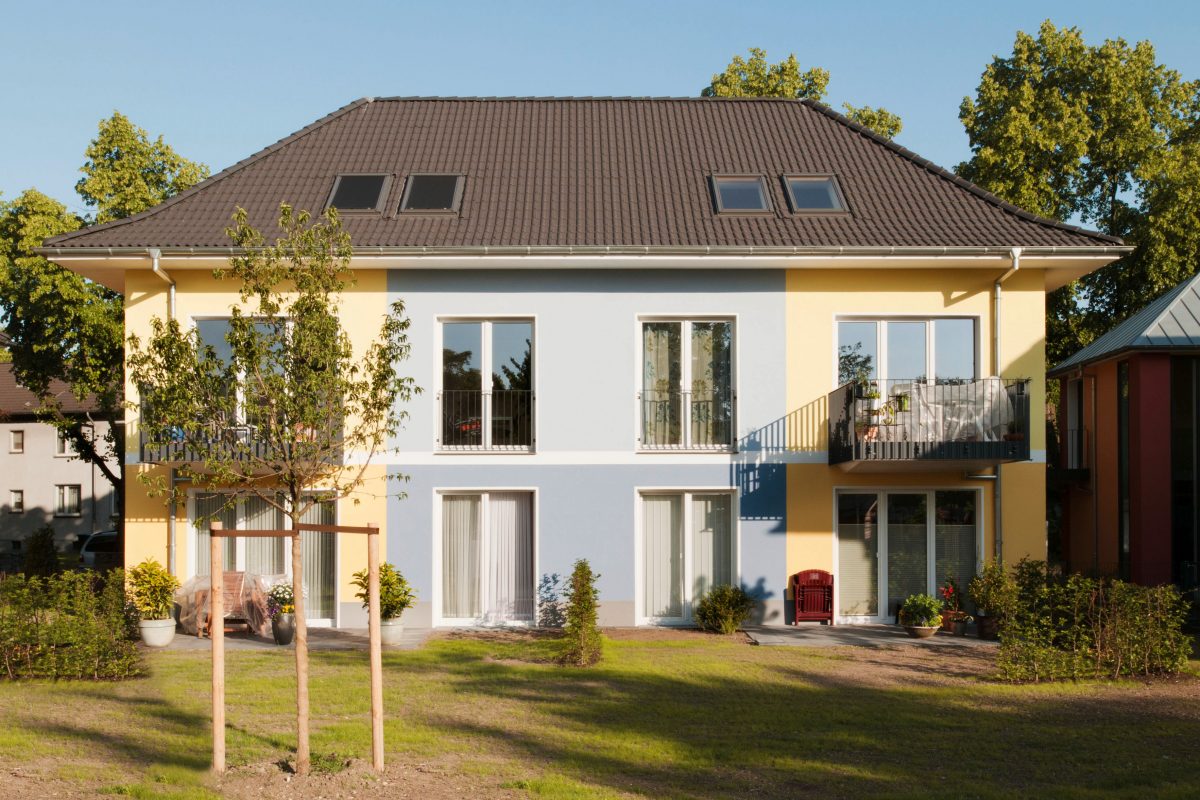 Zweifarbige Wohnhausfassade mit Balkonen und jungem Garten.