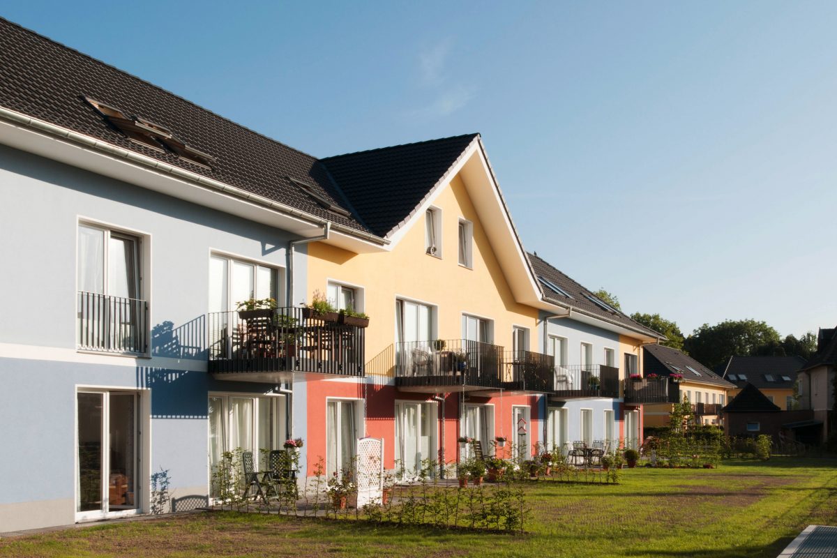 Mehrfamilienhaus mit Balkonen und farbiger Fassade bei Sonnenschein.