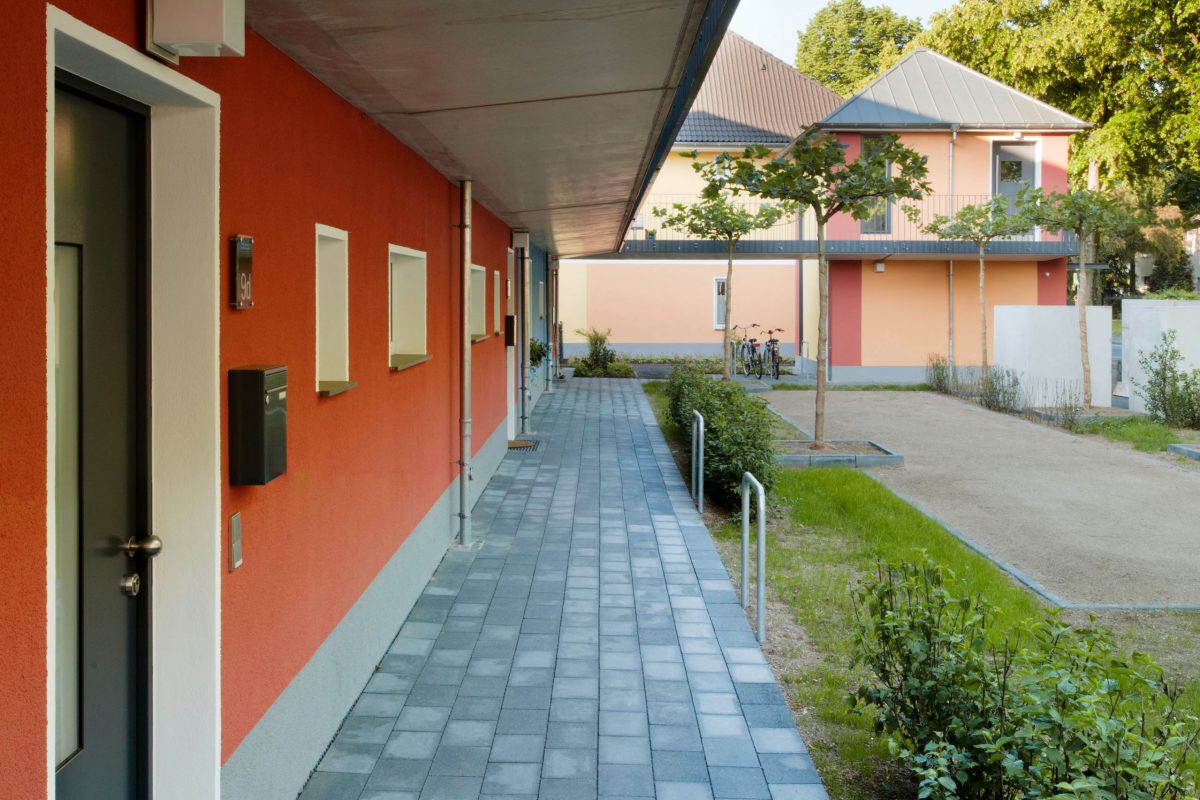 Barrierefreier Zugang entlang roter Hausfassade mit Vorgarten und Weg.