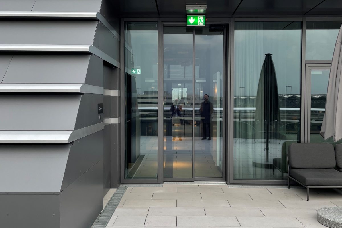 Moderner Ausgang auf die Dachterrasse mit Glastür, grauer Fassade und Sitzbereich außen.