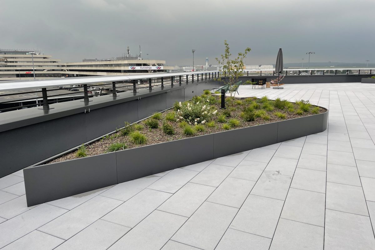 Dachterrasse mit Hochbeet, Sitzbereich und Blick auf das Flughafengelände.