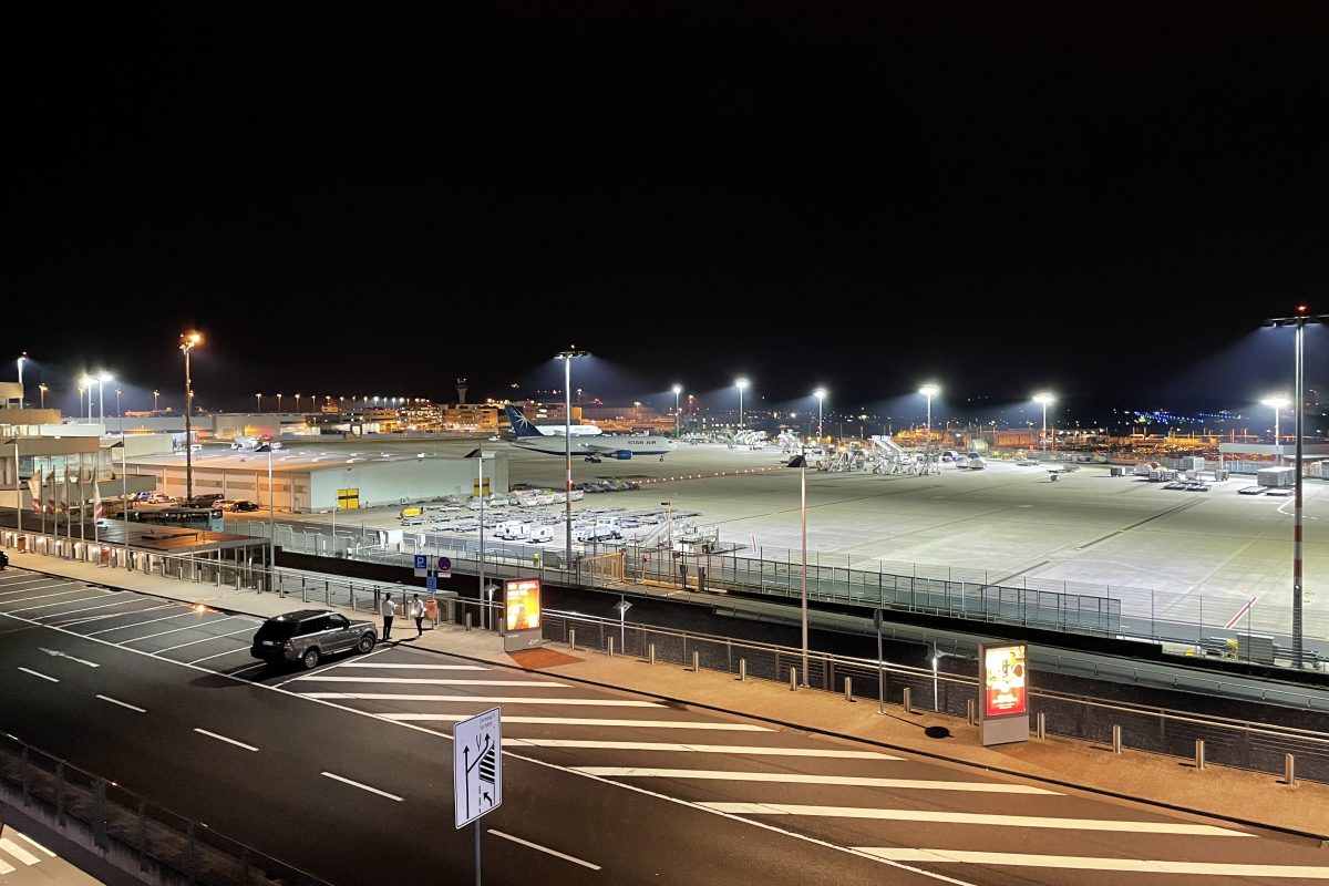 Blick von der Dachterrasse auf den Flughafen mit Rollfeld, Flugzeugen und heller Beleuchtung.