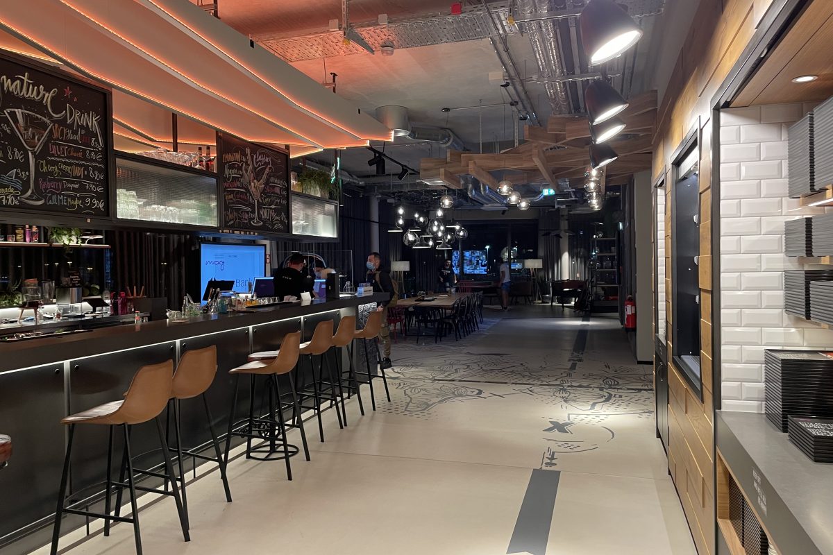 Moderne Bar mit Theke, Hockern und offener Deckenkonstruktion.