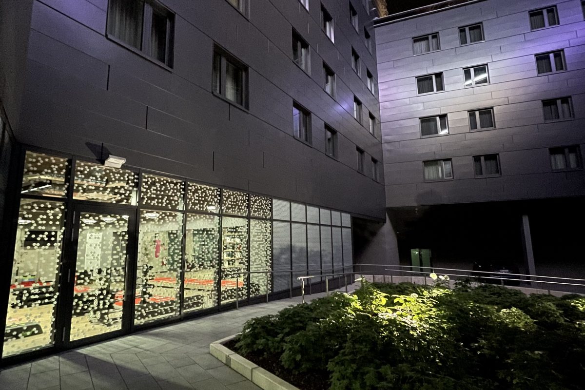 Beleuchteter Innenhof mit Pflanzenbeet, Glasfassade und Nachtstimmung.