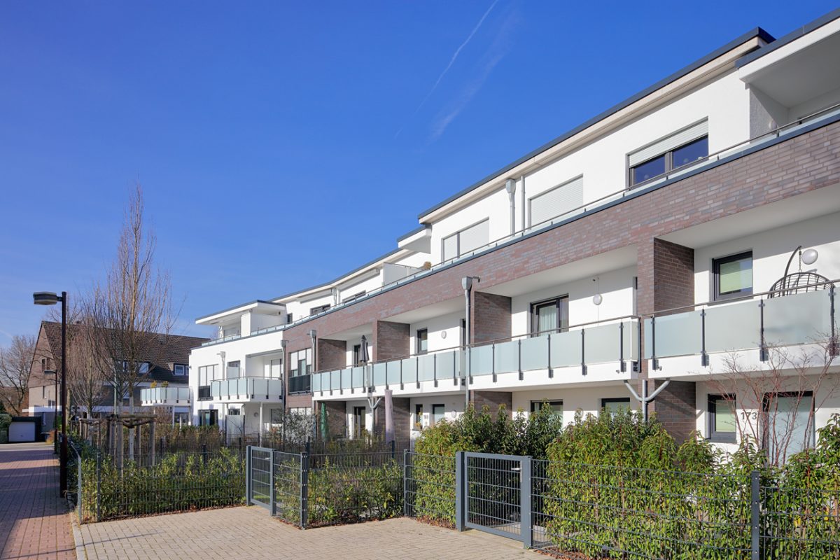 Modernes Wohngebäude mit Glasbalkonen und gepflegtem Vorgarten.