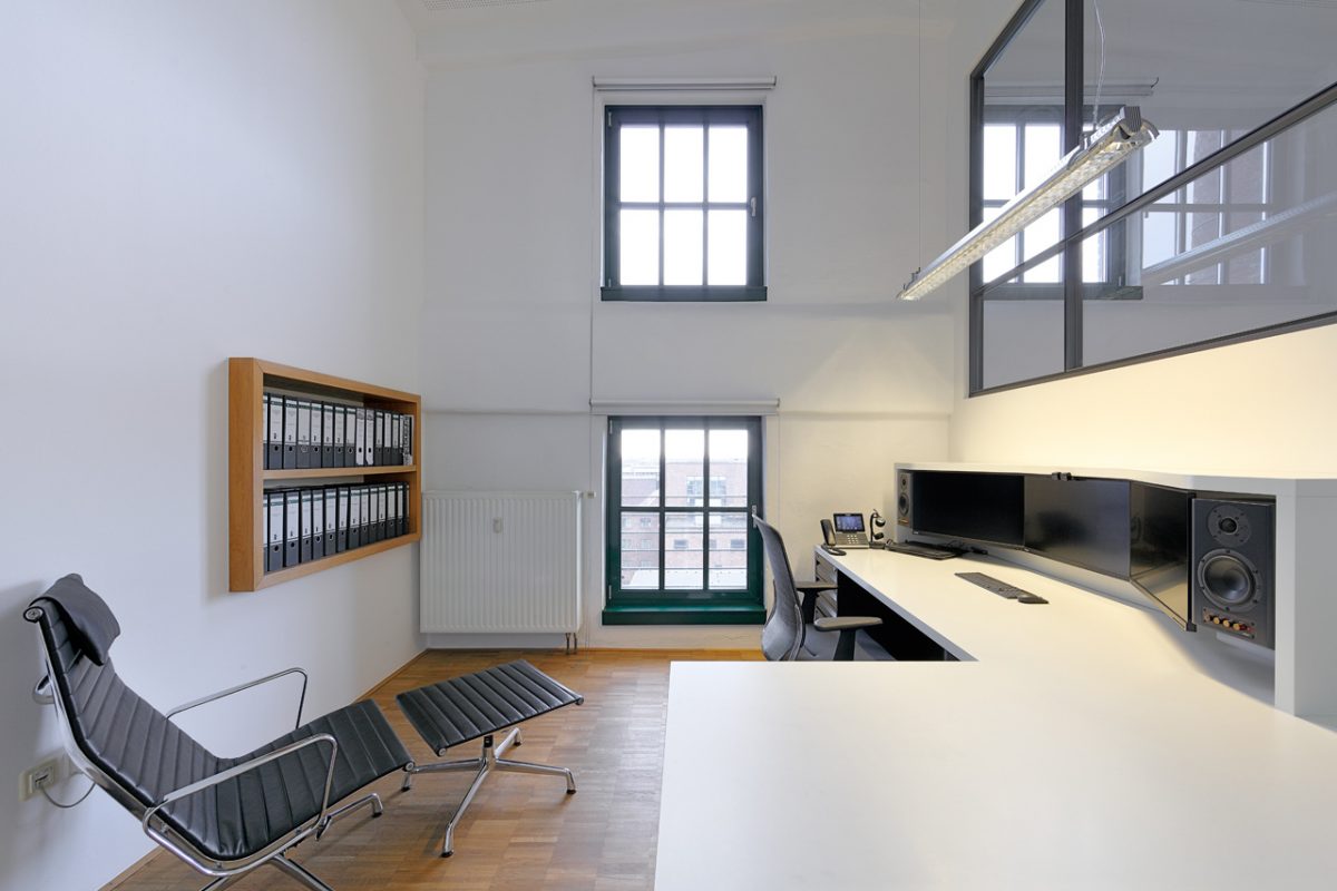 Modernes Büro mit hohen Fenstern, hellem Holzboden und ergonomischem Arbeitsplatz.