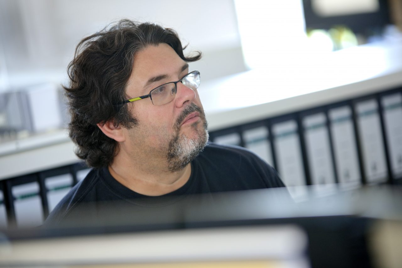 Mann mit Brille spricht konzentriert mit Kollegen am Arbeitsplatz.