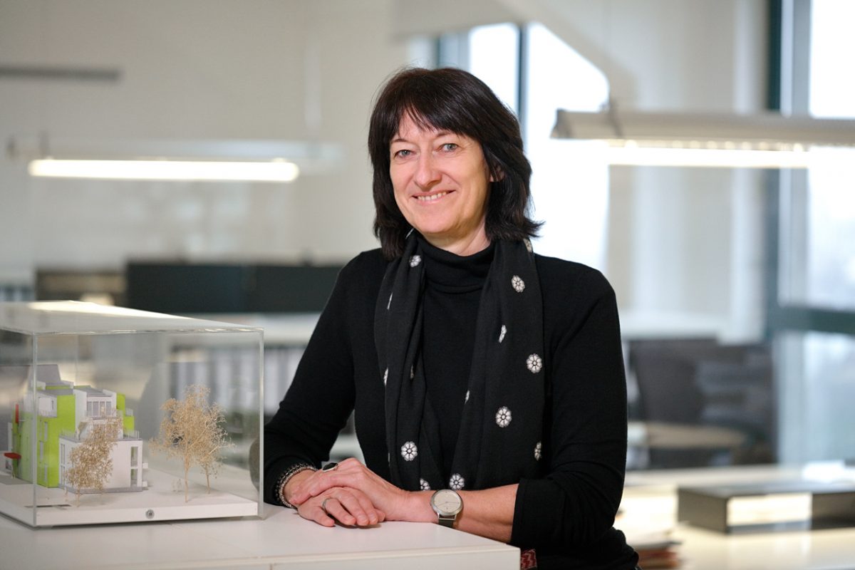 Frau im Büro lehnt an einem Architekturmodell in Vitrine und blickt lächelnd