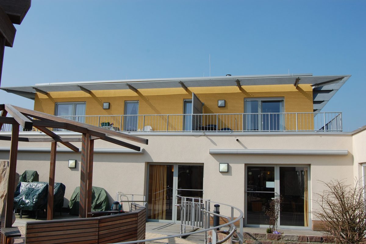 Moderne Dachterrasse mit Geländer und gelber Fassade im oberen Bereich.