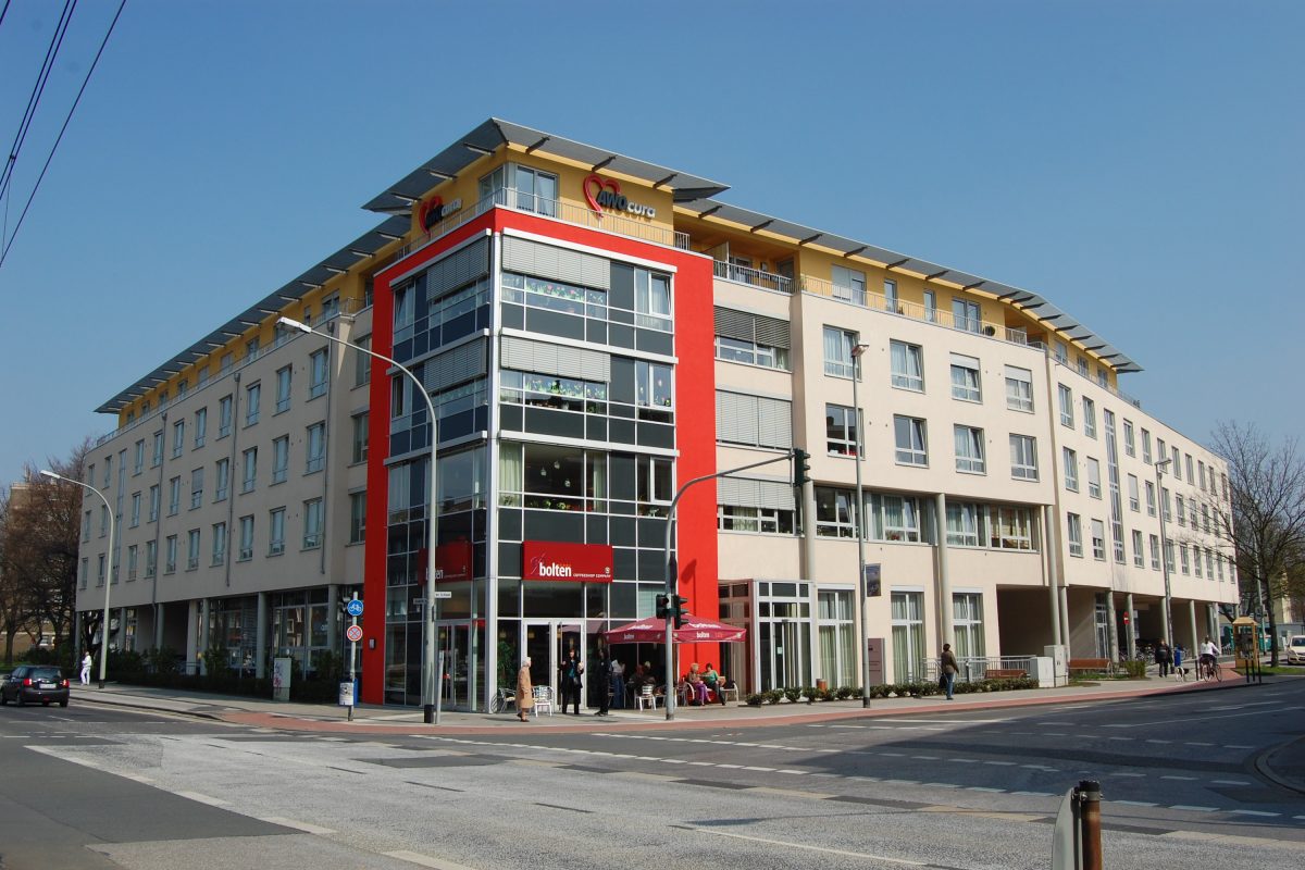 Modernes Eckgebäude mit „AWOcura“-Logo und Café im Erdgeschoss.