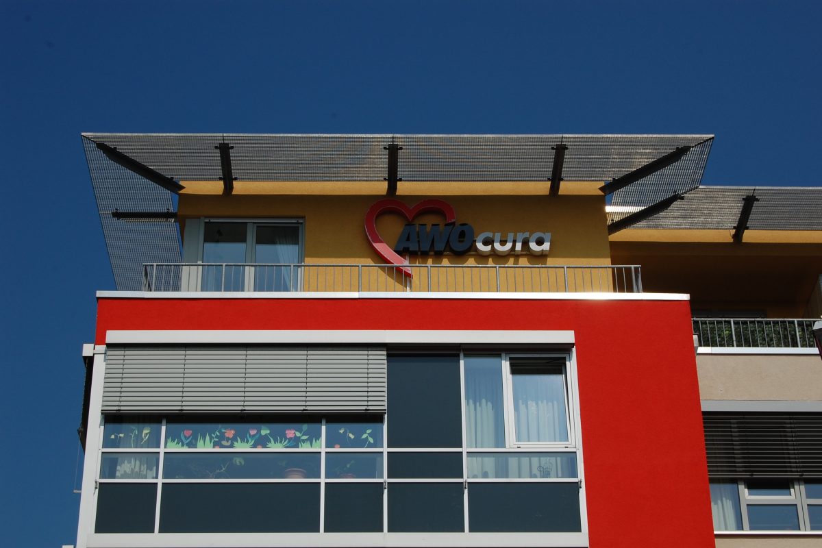 Fassadendetail mit Schriftzug „AWOcura“ und Herzsymbol.